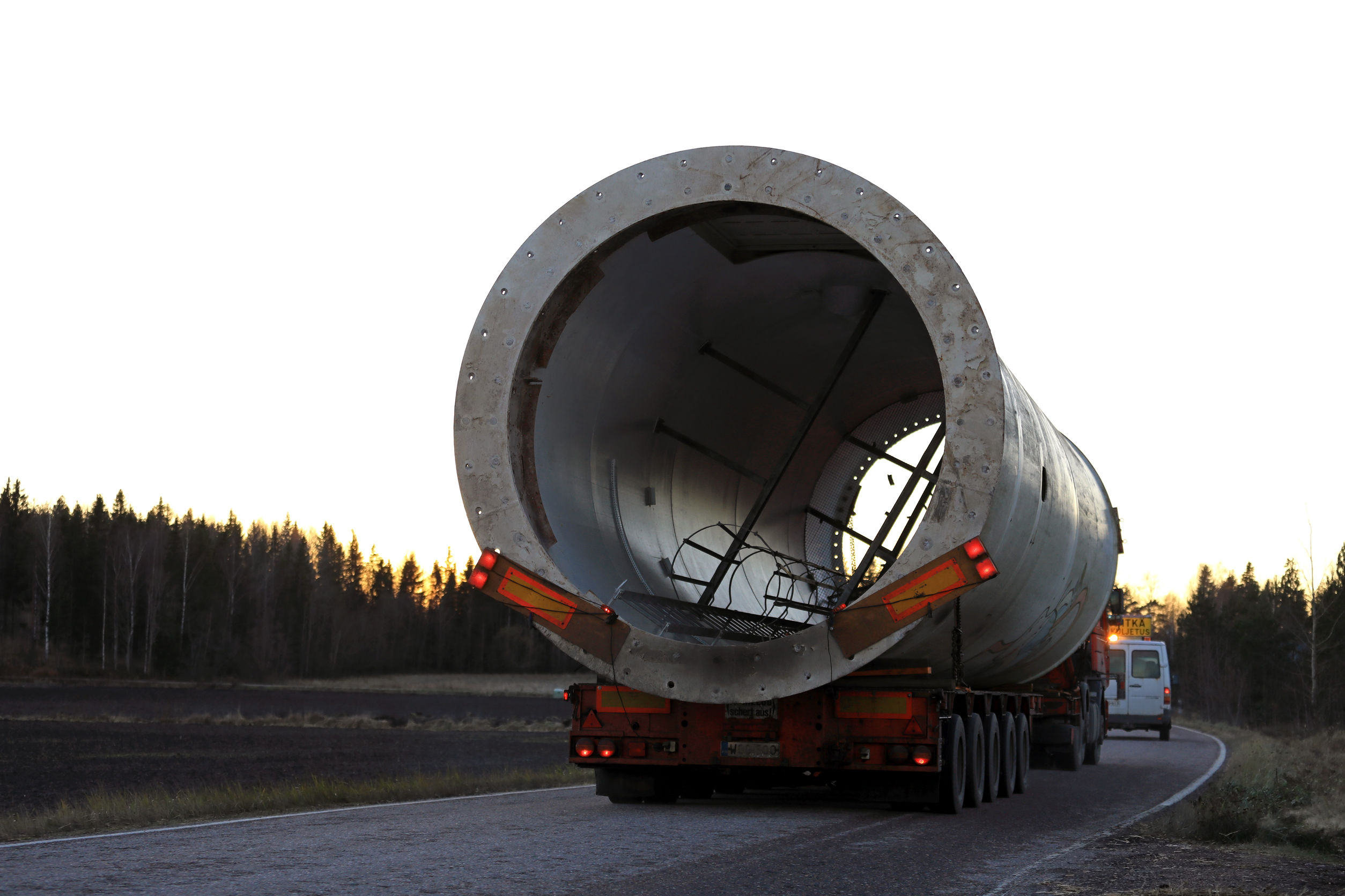 Oversize Load Transport at Sunset Oversize load transport of a wind turbine part and a pilot vehicle move along rural road.